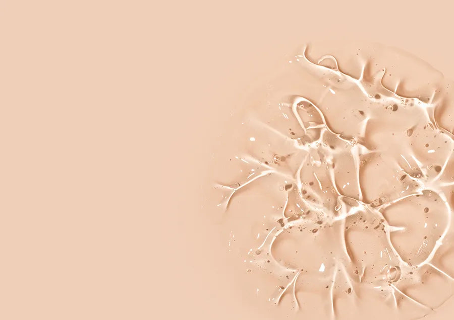 Close-up of beige liquid foundation or makeup smeared on a light beige surface, with textured, glossy, and slightly marbled patterns on the right side, while the left side is empty.