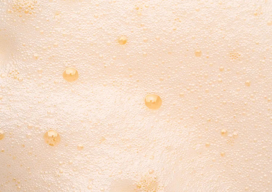 Close-up image of light beige foam with bubbles of various sizes scattered across the surface.