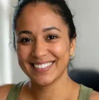 A woman with dark hair pulled back smiles at the camera. She is wearing a green top and small hoop earrings, and the background is softly blurred.