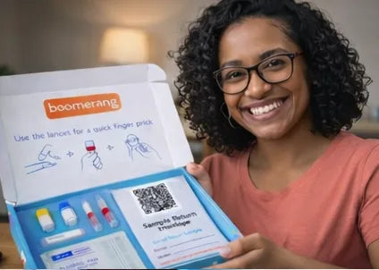 A smiling woman with curly hair and glasses holds an open kit labeled "boomerang," containing medical supplies and instructions for using a lancet for a finger prick blood test.