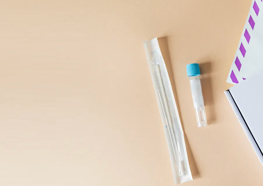 A DNA test kit with a sealed cotton swab and a small vial with a blue cap, placed on a beige surface next to an envelope and a box.