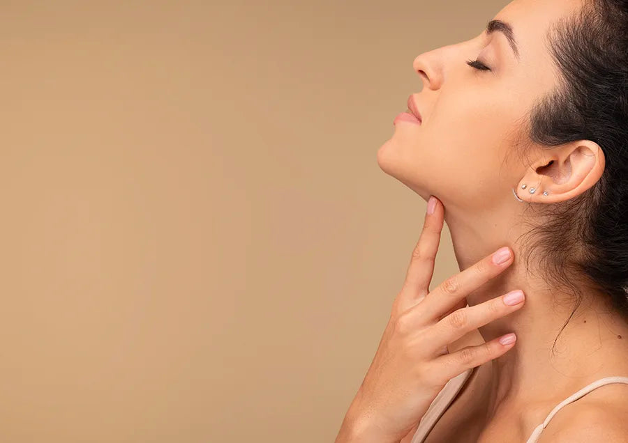A woman with her eyes closed gently touches her neck with her fingers. She has a calm expression and is shown in profile against a plain beige background.